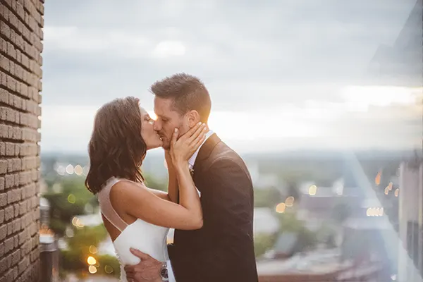 Married couple kissing on the rooftop with city skyline behind them.