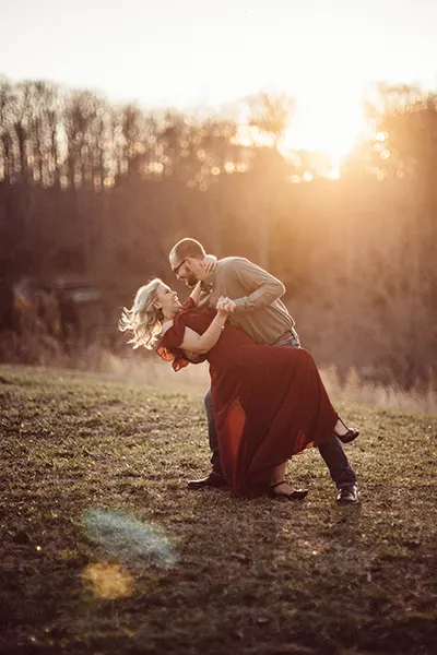 Woman in a red dress dancing with fiance under the sunset